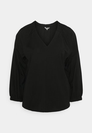 Blouse noire avec col en V, manches longues bouffantes et détails froncés aux épaules. Réalisée en tissu léger, elle présente une coupe décontractée.