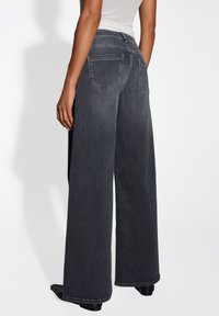 Wijdvallende donkergrijze jeans van denim, met twee achterzakken en een hoge taille. De stof heeft een gladde textuur en zichtbare stikdetails.