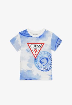 T-shirt tie-dye blanc et bleu avec logo triangle GUESS contour rouge et motifs de tampons circulaires bleus sur le devant et les manches.