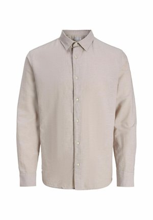 Noor lok sirgete lokkidega, seljas beežist nööpidega särk musta graafilise T-särgi peal, mustad laiade säärega teksad ja valged tossud, vaatab paremale.