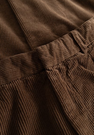 Close-up of brown corduroy fabric with visible vertical ridges and a folded waistband detail.