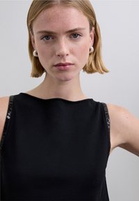 Top negro sin mangas con tirantes brillantes y adornados. La tela tiene una textura suave, con un diseño sencillo y moderno.