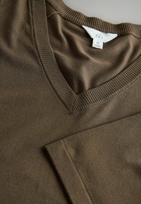 Brauner V-Ausschnitt-Pullover aus weichem, glattem Stoff. Mit geripptem Kragen und Bündchen, wobei ein ordentlich gefalteter Ärmel sichtbar ist. Größenetikett: M.