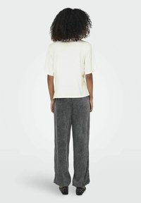 Kortærmet creme top parret med grå brede bukser med sideslids og sort nittet fodtøj. Glat tekstur, afslappet design.