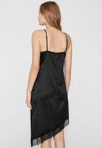 Vestido lencero de satén negro con tirantes delgados ajustables, con un ribete de encaje en forma de ondas en el dobladillo. Textura suave, diseño de longitud media.