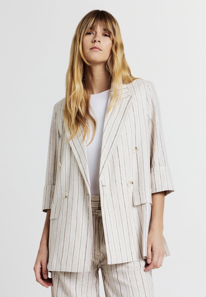 Blazer double boutonnage rayé en beige clair avec des rayures verticales. Présente une coupe ajustée, des revers crantés et des manches retroussées.