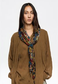 Bufanda multicolor con un patrón hecho de tela ligera, atada alrededor del cuello, que presenta diseños vibrantes en tonos azules, rojos y verdes.