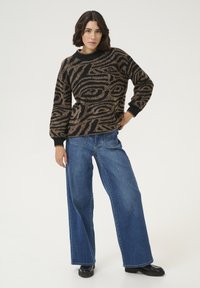 Pulover cu model maro și negru, cu guler rotund, asociat cu blugi largi de culoare albastră și pantofi negri. Textură netedă și croială confortabilă.