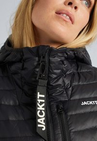 Svart puffjacka med dragkedjeslutning och justerbar huva. Har quiltad textur och framträdande "JACK1T"-logotyp på dragkedjestroppen.