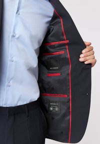 Granatowa marynarka z gładką, teksturowaną podszewką z czerwonymi akcentami oraz wieloma kieszeniami; metka wskazuje na "PERSONAL FIT".