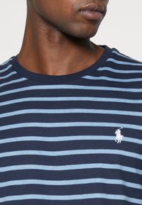 Navy blue and light blue striped t-shirt with a crew neck and short sleeves; features a small white embroidered logo on the chest.