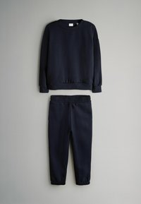 Dunkelblaues Sweatshirt und passende Jogginghose mit elastischem Bund flach auf einem hellgrauen Hintergrund ausgelegt.