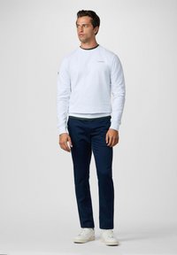 Sudadera azul claro con cuello redondo y logo, combinada con pantalones ajustados azul oscuro. Zapatillas blancas completan el conjunto.