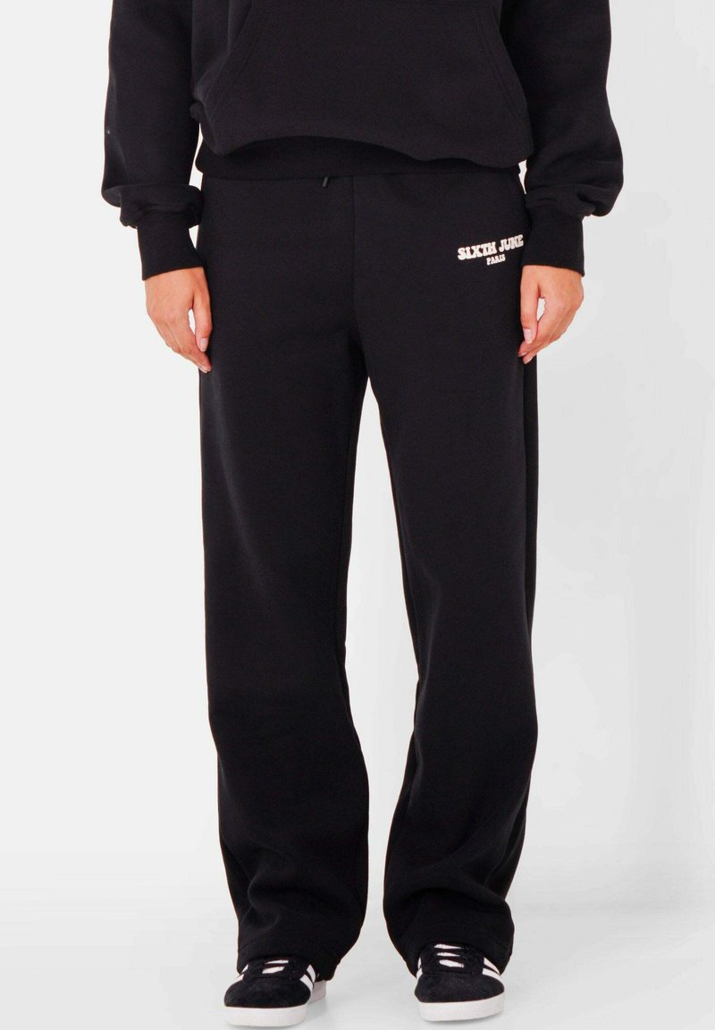 Zwarte joggingbroek met witte tekst "SIXTH JUNE". Gemaakt van zacht materiaal, met een relaxed fit en een elastische tailleband. Glad textuur, geen patronen.