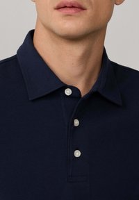 Granatowa koszulka polo z bawełny z klasycznym kołnierzykiem, trzema białymi guzikami oraz subtelnymi detalami w szyciu. Miła w dotyku.