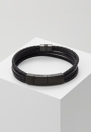 Black multi-strand braided and smooth leather bracelet with sleek black magnetic clasp placed on white geometric pedestal.