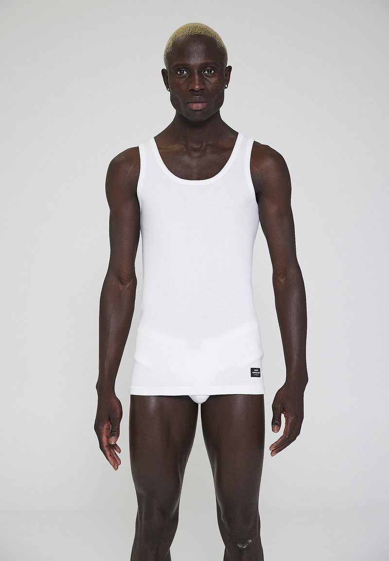 White cotton tank top with a round neckline and a fitted design. The fabric is smooth, and a label is positioned at the bottom left.