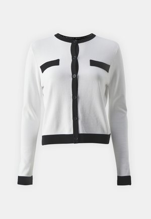 Gilet blanc en tissu doux, avec des accents noirs, un col rond, une fermeture à boutons et deux poches poitrine.