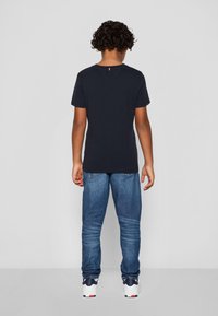 T-shirt in cotone blu scuro con maniche corte, abbinato a jeans in denim blu chiaro. La maglietta presenta un piccolo accento rosso sul collo.