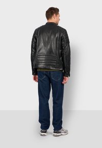 Černá kožená bunda s žebrovanými akcenty na ramenou, zadními kapsami a rovnými linemi. Model má na sobě modré džíny a tenisky.