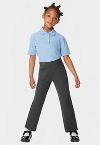 Polo a maniche corte azzurro chiaro con tre bottoni, abbinata a pantaloni aderenti grigio scuro, con una texture liscia. Scarpe nere indossate.