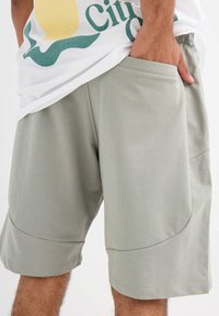 Pantalones cortos verdes claros de tela suave con un corte relajado. Presentan bolsillos laterales y costuras decorativas a lo largo de las piernas.