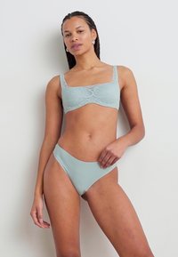 Fénykék bikini szett, amely textúrázott csipkebrából készült, széles pántokkal és passzoló, magasan szabott alsó résszel, mindez sima anyagból.