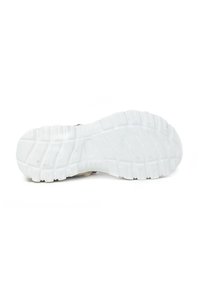 Suela de goma blanca de un zapato con profundas ranuras y superficie texturizada, parcialmente oculta por una parte superior beige. Sin marcas visibles.