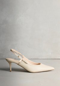 Smėlio spalvos odiniai smailiais noseliais slingback bateliai su plonu kulnu. Turi reguliuojamą dirželį ir lygų paviršių su toniniu siuvimu.