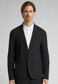 Svart blazer i lättviktsmaterial med två framfickor, slagkrage och tvåknappsstängning. Slät textur och skräddarsydd passform.