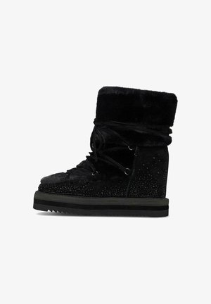 Botas negras hasta el tobillo con textura de ante, cuello forrado de piel, cordones en la parte delantera y detalles de tachuelas en los laterales. Suela de goma con patrón de zigzag.