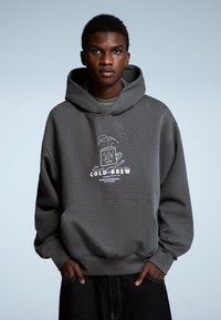 Grijze hoodie met een gestructureerd oppervlak, een grote voorzak en een geborduurde "COLD-BREW" afbeelding. Voorzien van een capuchon met trekkoorden en een ontspannen pasvorm.