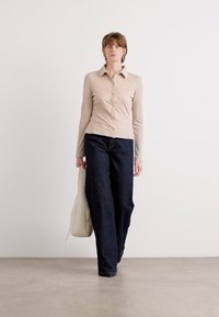 Beige gestreifte Langarmbluse mit Kragen, kombiniert mit locker sitzenden dunklen Jeans. Das Model trägt eine hellfarbige Tasche.