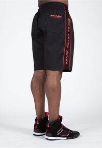 Schwarze Sportshorts aus strukturiertem Stoff mit roten vertikalen Streifen und "GORILLA WEAR"-Branding, kombiniert mit schwarz-roten High-Top-Sneakern.