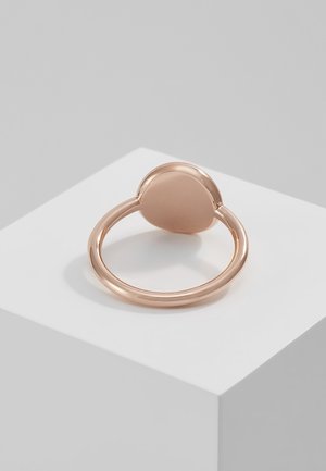 Simple polished rose gold ring with a smooth oval top resting on a white cube against a gray background.