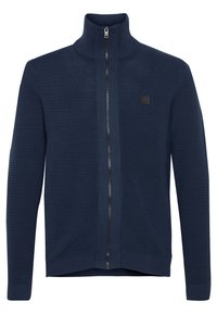 Mornarsko plava zip-up i majica s visokim ovratnikom, teksturirani rebrasti dizajn i crna munja. Ima malu oznaku na prednjem dijelu.