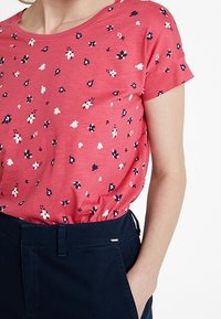 Camiseta de manga corta rosa con escote redondo y un patrón floral en blanco y navy. Combinada con pantalones azul oscuro.