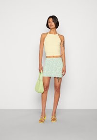 Top cropped amarelo com alças, saia mini floral azul claro, bolsa tecida verde, saltos amarelos com tiras. Texturas suaves, cores vibrantes.