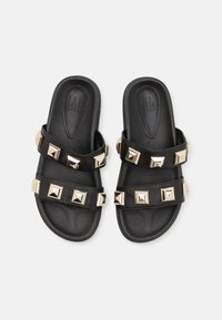 Sandales noires à glisser avec deux larges sangles ornées de clous en métal doré en forme de pyramide. Matériau en cuir lisse avec une semelle intérieure rembourrée.