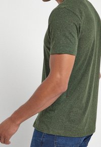 Grøn, kortærmet T-shirt med struktureret stof og en klassisk pasform, vist fra en sideperspektiv mod en lys baggrund.