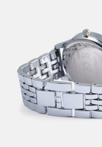 Sølv rustfritt stål klokke med lenkearmbånddesign. Har en glatt metallfinish og et rundt hus med en teksturert krone.