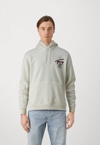 Lichtbeige hoodie met een kangoeroezak, een capuchon met trekkoord en een geborduurd logo in rood en marineblauw. Zacht materiaal met geribbelde manchetten.