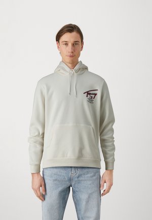 Sudadera color beige claro con un bolsillo tipo canguro, capucha con cordón y logo bordado en rojo y azul marino. Tela suave con puños de canalé.