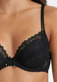 Mustat pitsiset bralette, jossa on kukkakirjonta, säädettävät hihnat ja pieni nauha keskellä, sekä aaltoreunus vyötäröllä.