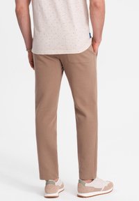 Beige, schmal zulaufende Hose mit glatter Textur, ausgestattet mit einer Gesäßtasche und kombiniert mit hellen Sneakern. Lässiges Design, geeignet für den Alltag.