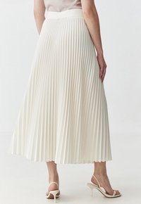 Gonna midi plissettata di colore crema con un ampio cinturino in vita. Texture liscia e design fluido, caratterizzata da pieghe verticali e un orlo che ondeggia dolcemente.