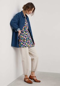 Jeansowa kurtka, sukienka w kwiatowe wzory w żywych kolorach, kremowe spodnie i brązowe buty o fakturze. Prosty, funkcjonalny design z kontrastującymi elementami.