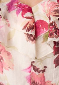 Bloes met bloemenprint en gerimpelde halslijn; heeft roze en bordeauxrode bloemen op een licht crème achtergrond; lichtgewicht, gestructureerde stof.