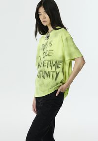 Camiseta de gran tamaño en color verde neón con texto en spray negro que dice "ESTA ES UNA OPORTUNIDAD ÚNICA EN LA VIDA." Combínala con pantalones negros. Tejido de algodón.