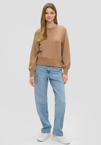 Bruine trui met lange mouwen, ronde halslijn en geribbelde zoom, gecombineerd met lichtblauwe denim jeans en witte sneakers.